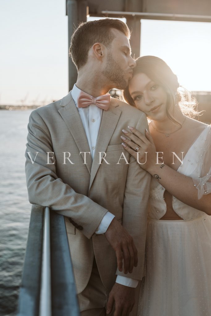 Bräutigam gibt Braut einen Kuss auf die Stirn. Auf dem Bild steht "VERTRAUEN"