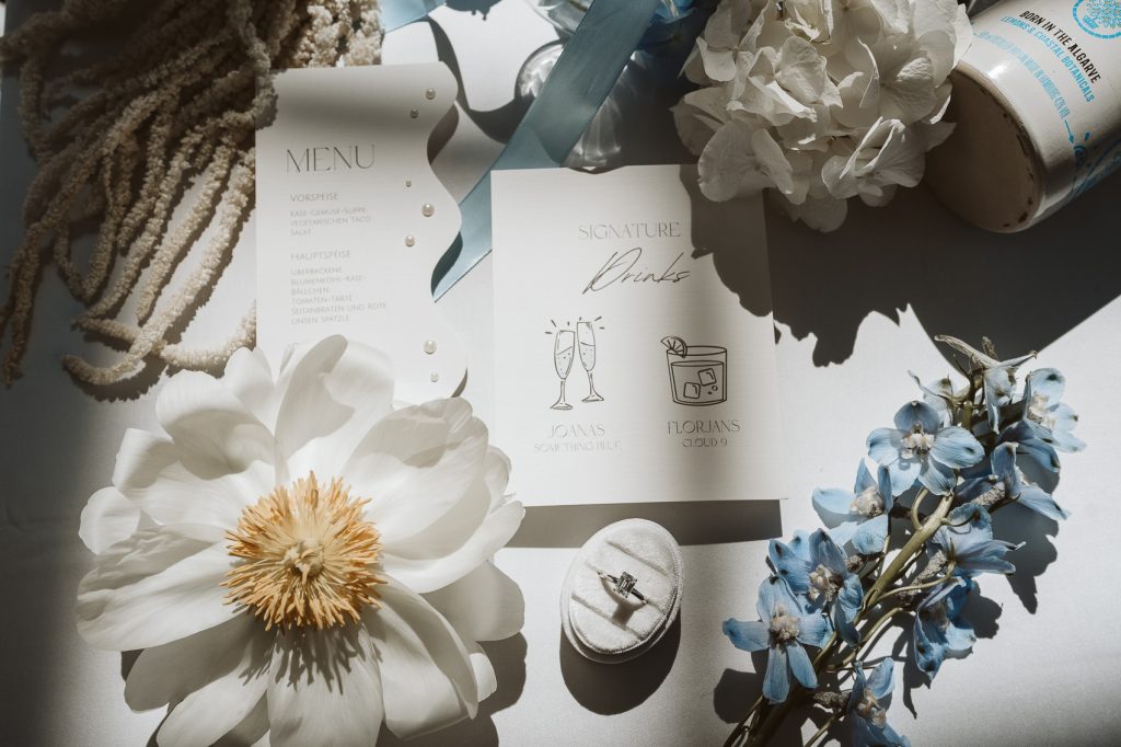 Hochzeitspapeterie, Eheringe und weiße Blumen auf einem Tisch